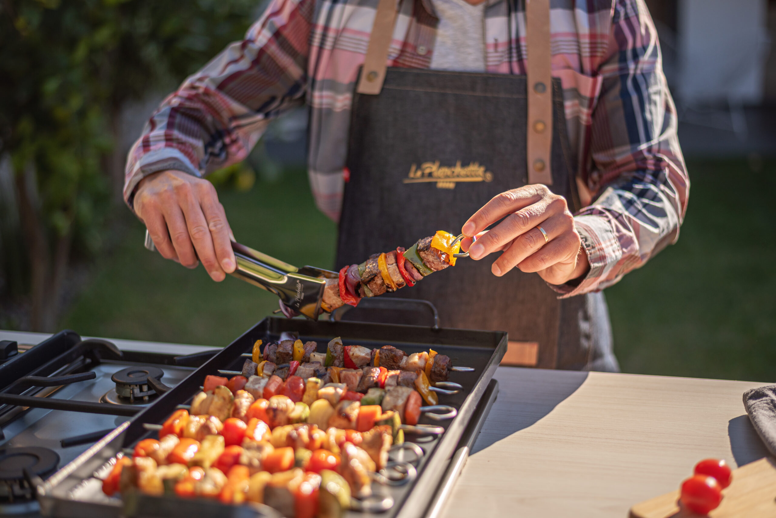 hombre cocinando brochettes en la planchetta de 2 hornallas con los pinchos y la pinza